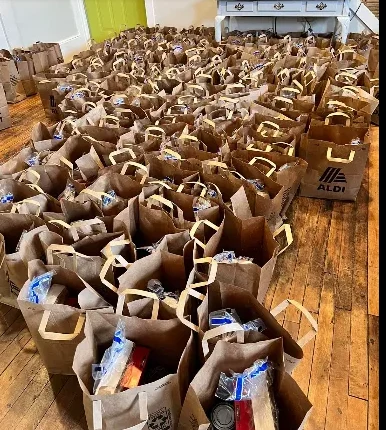 Paper grocery bags packed with food and lined up on a wood floor, ready to be given to neighbors in need