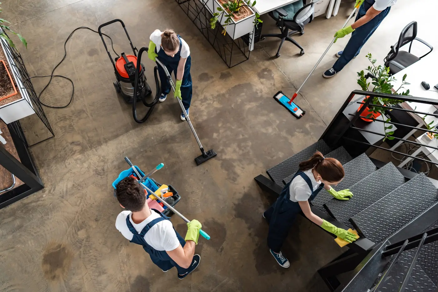 A cleaning crew vacuuming, mopping and wiping stairs in an open-plan office, seen from above